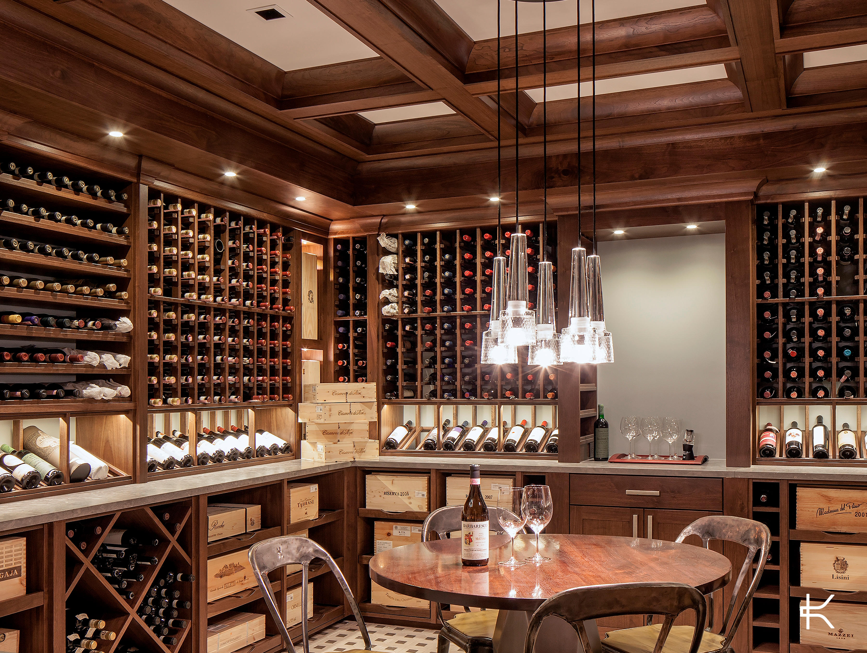 Traditional wood-panelled cellar with floor-to-ceiling individual racking and case bins, a tasting table at the centre beneath a multi-pendant fixture