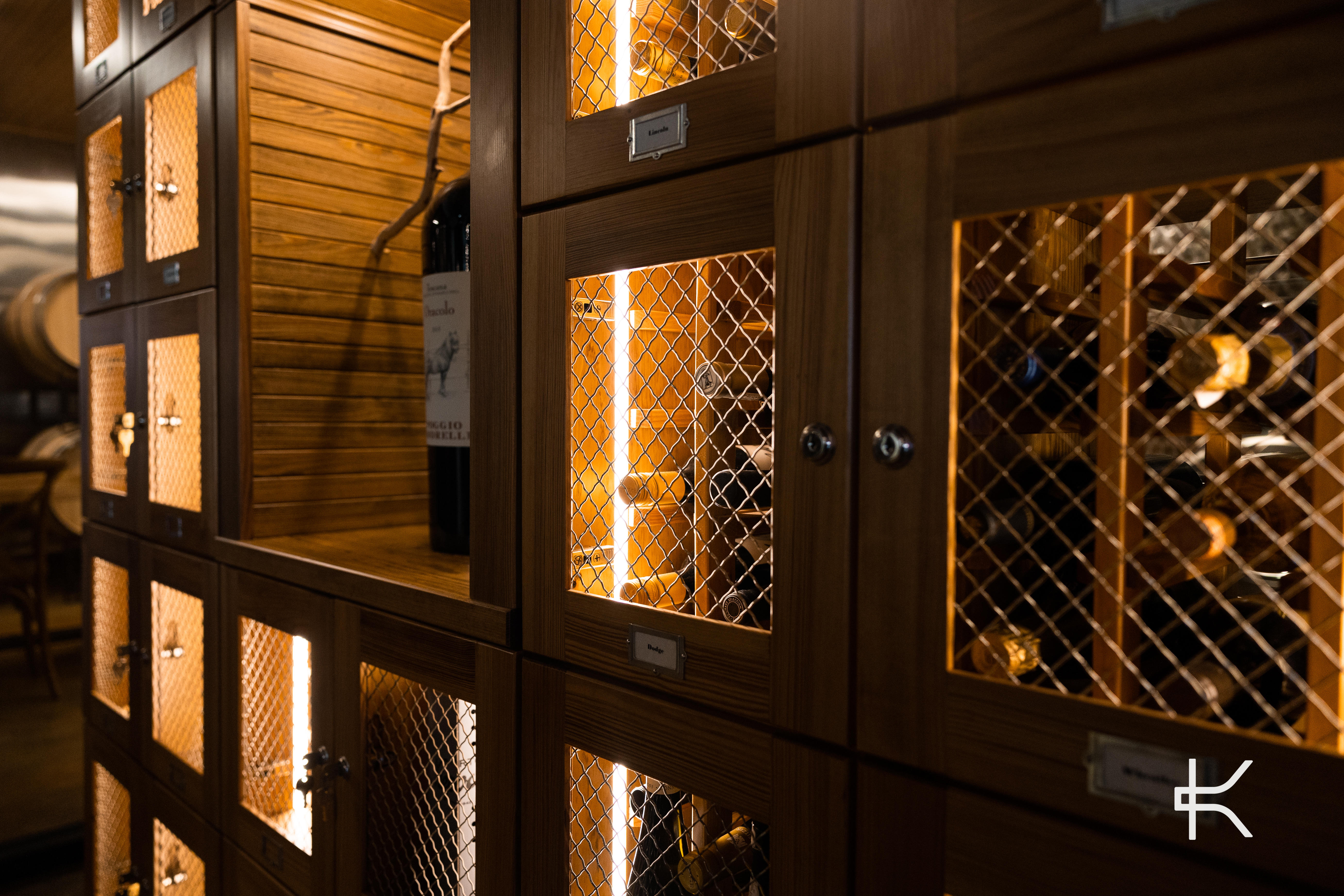 Close detail of wood locker fronts with woven metal mesh doors, backlit so the bottles inside read as silhouettes