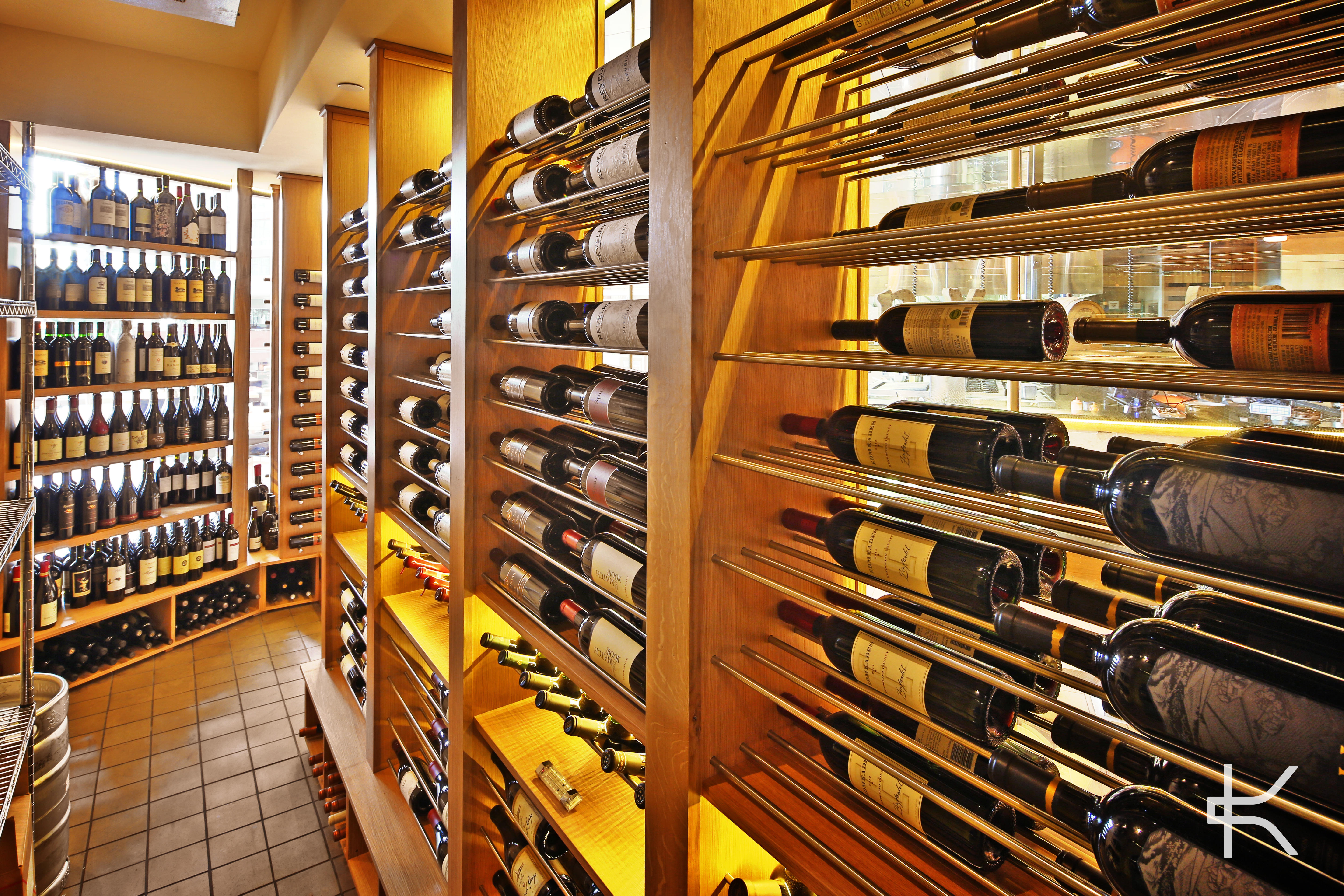 Storage aisle combining wood shelving with metal rod racking, bottles held both label-forward and cork-out under warm light