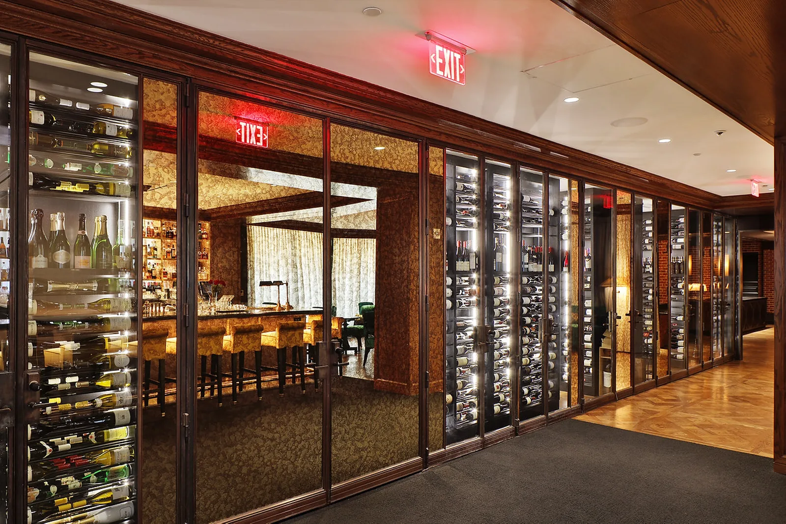 Hospitality wine corridor lined with glass-fronted, temperature-controlled cabinets framing a private dining bar beyond